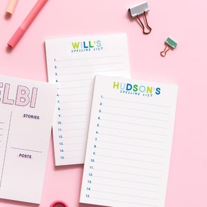 May include: Two white notepads with blue and green lines. The top notepad has the text "WILL'S SPELLING LIST" in colorful letters. The bottom notepad has the text "HUDSON'S SPELLING LIST" in colorful letters. Both notepads have numbers 1-15 listed on the left side.
