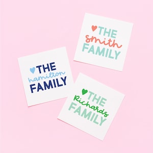 May include: Three white square cards with the text "THE" in a light blue heart, followed by a family name in a colorful font, and then "FAMILY" in a light blue font. The names are "hamilton", "smith", and "richards".
