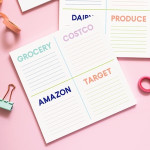 May include: A white notepad divided into five sections with headings: Grocery, Amazon, Costco, Target, and Produce. Each section has lined spaces for writing.
