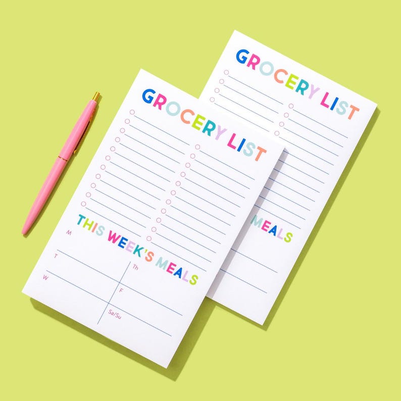 May include: Two white grocery list pads with colorful text. The top pad says "Grocery List" and the bottom pad says "Grocery List" and "This Week's Meals". The bottom pad has a section for each day of the week.