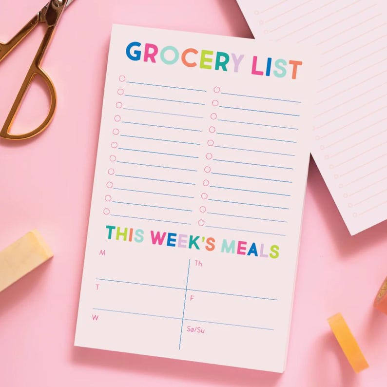 May include: A white notepad with a colorful "Grocery List" heading and a section for "This Week's Meals". The notepad has lines for writing and checkboxes for marking items off the list.