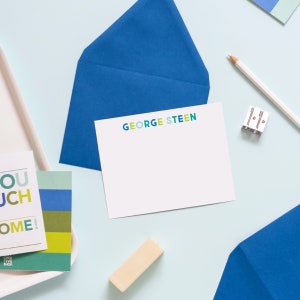 May include: A white card with the text "GEORGE STEEN" in colorful letters. The card is on a blue background with a blue envelope and a white pencil.