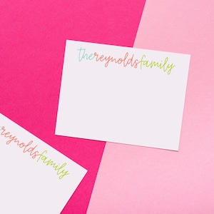 May include: Two white note cards with the text "thereynoldsfamily" written in colorful script on each card. The cards are on a pink and fuchsia background.