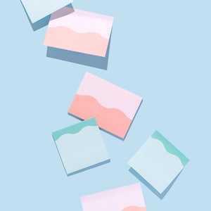 May include: A collection of rectangular sticky notes arranged on a light blue surface. The notes feature a wavy horizontal line pattern, with some displaying a pink and light peach color scheme, while others show a light green and white design.