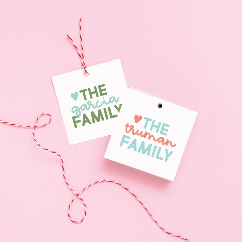 May include: Two white gift tags with red string. The top tag says "THE garcia FAMILY" in green and white lettering with a small red heart. The bottom tag says "THE truman FAMILY" in blue and white lettering with a small pink heart.