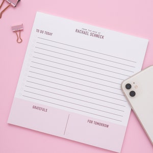 May include: A white to-do list notepad with pink accents. The notepad has sections for "To Do Today", "Gratefuls", and "For Tomorrow". The notepad also has the text "From the desk of Rachael Schneck" at the top.