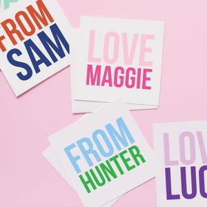May include: Four colorful square cards with text. The top card is red and orange and says "FROM SAM". The second card is pink and says "LOVE MAGGIE". The third card is blue and green and says "FROM HUNTER". The fourth card is purple and says "LOVE LUC"