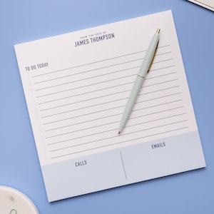 May include: A white notepad with blue lines and a blue header that says "TO DO TODAY". The header also says "FROM THE DESK OF JAMES THOMPSON". The notepad is divided into two sections, one labeled "CALLS" and the other labeled "EMAILS". A light blue pen is lying on the notepad.