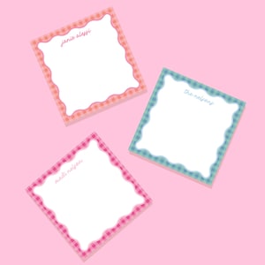 May include: Three square notepads with scalloped edges and gingham borders in pink, orange, and blue. Each notepad has a white interior and a name written in cursive. The background is a solid pink color.