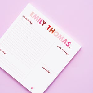 May include: A white notepad with the name "EMILY THOMAS" in pink, red, and orange lettering. The notepad has sections for "To do today," "Calls & emails," "Notes," and "Reminders." A small pink heart is at the bottom.