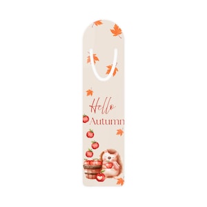 Könnte beinhalten: Beige Lesezeichen mit weißer Schlaufe und herbstlichen Illustrationen. Das Design umfasst orangefarbene Blätter, rote Äpfel und einen Igel, der einen Apfel hält. Der Text "Hello Autumn" ist in roter Schrift geschrieben.