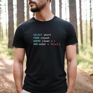 May include: Black t-shirt featuring the text "SELECT shirt FROM closet WHERE clean = 1 AND color = 'Black';" in a colourful, code-like font. The shirt has a classic crew neck.