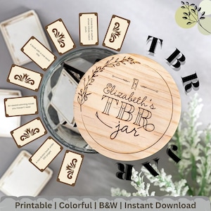May include: A wooden lid with the text "Elizabeth's TBR jar" sits atop a glass jar surrounded by small cards with book prompts. The lid has a decorative floral design. The cards have prompts like "A book with a one-word title."