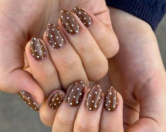 May include: Almond-shaped fingernails painted with a glossy dark brown polish featuring small, evenly spaced white polka dots. The nails are groomed to a smooth, rounded point, showcasing a consistent pattern across all ten fingers in this manicure.