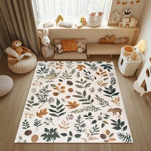 May include: A white play mat with a woodland pattern featuring green leaves, brown acorns, and a small brown animal. The mat is on a wooden floor in a nursery.