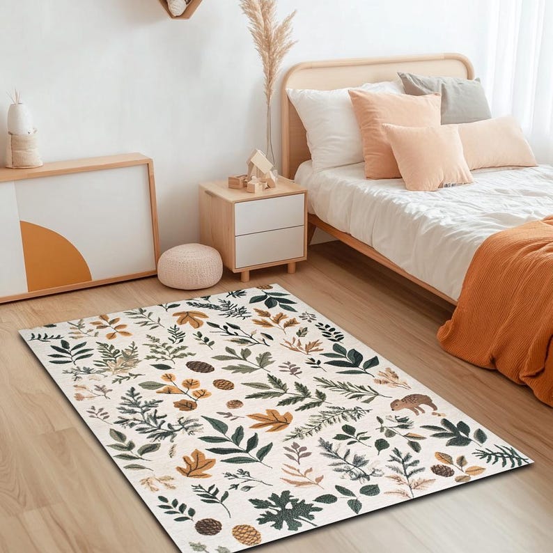 May include: A white area rug with a pattern of green and brown leaves and branches. The rug is on a wooden floor in a bedroom with a bed and bedside table.
