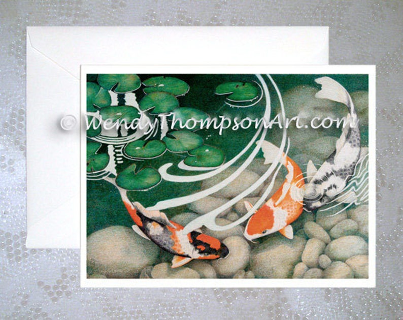 May include: Two koi fish swim in a pond with lily pads and rocks. The koi are orange, white, and black. The water is clear and blue. The pond is surrounded by green lily pads.