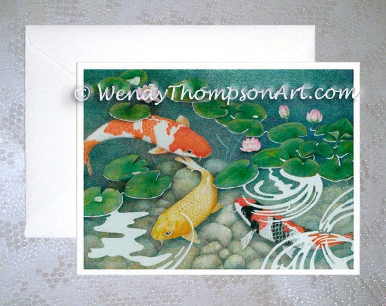 May include: A watercolor painting of three koi fish swimming in a pond with lily pads and pink flowers. The fish are orange, yellow, and black and white.