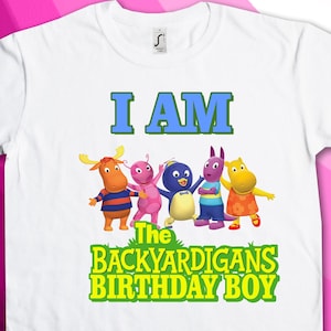 May include: White t-shirt featuring the text "I AM The Backyardigans Birthday Boy" in green and yellow. The characters Uniqua, Pablo, Tyrone, Tasha, and Austin from the children's television show Backyardigans are depicted on the shirt.