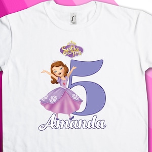 Puede incluir: Camiseta blanca con un diseño morado y azul con Sofía la Primera, un número 5 y el nombre Amanda.