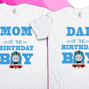 Puede incluir: Dos camisetas blancas con texto azul y un tren de dibujos animados. La camiseta de la izquierda dice "Mamá del niño de cumpleaños" y la camiseta de la derecha dice "Papá del niño de cumpleaños".