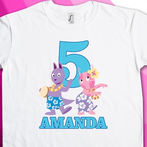 Könnte beinhalten: Weißes T-Shirt mit einer blauen Zahl 5, zwei Comicfiguren, die hawaiianische Blumenketten tragen, und dem Namen "AMANDA" in blauen Buchstaben.