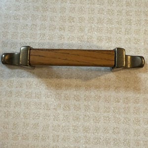 Puede incluir: Un tirador de armario de madera con un centro de madera marrón y extremos de metal plateado.