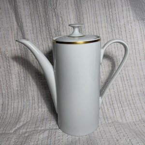 May include: A tall white porcelain coffee pot with a cylindrical body, a long slender spout, and a curved handle. The lid features a small knob handle and is accented with a thin gold band around the rim, matching the gold trim on the pot's top.