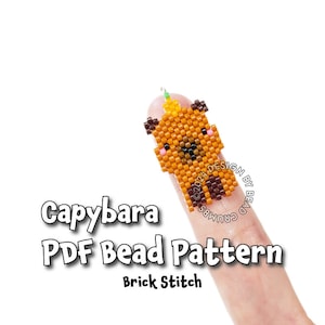 May include: A beaded capybara charm in shades of brown, orange, and black, with a small green accent. The charm is made using the brick stitch technique. Text on the image reads "Capybara PDF Bead Pattern Brick Stitch".
