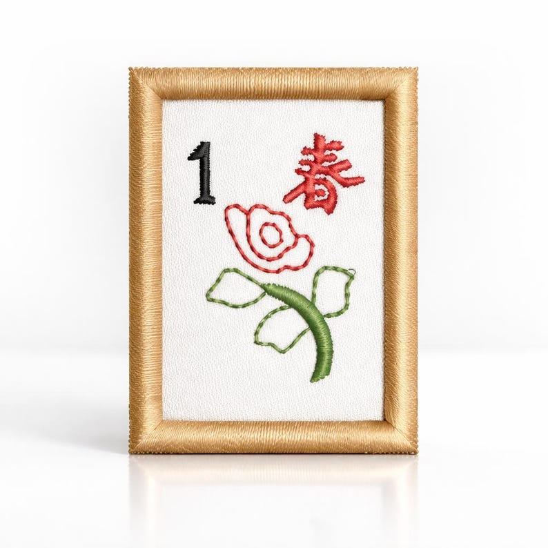 May include: A framed Mahjong tile with the number 1 in black, a red Chinese character, and a red and green floral design. The frame is a light brown colour.