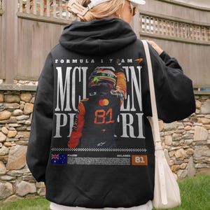 May include: Black hoodie featuring a Formula 1 design. The back displays "MCLAREN PIASTRI" in large white letters, with a driver graphic and the number 81. The design includes the Australian flag and the McLaren logo.