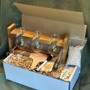 May include: A wooden propagation station kit with three glass bulb vases. The kit includes a wooden plant marker, a marker, a small bag of white pebbles, and other items, all inside a white box with a cardboard lid.