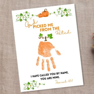 Peut inclure: Impression d'art blanche avec un motif d'empreinte de main. L'impression présente le texte "Dieu m'a cueilli du champ" et "Je t'ai appelé par ton nom, tu es à moi". L'empreinte de main est orange, avec des illustrations de citrouilles et de vignes.