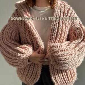 Puede incluir: Un cárdigan de punto rosa con un patrón de punto de cable grueso. El cárdigan tiene cuello en V y mangas largas. El texto "DOWNLOADABLE KNITTING PATTERN" es visible en el cárdigan.