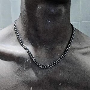 May include: A silver chain necklace with a curb link design. The necklace is worn by a person with a bare chest.