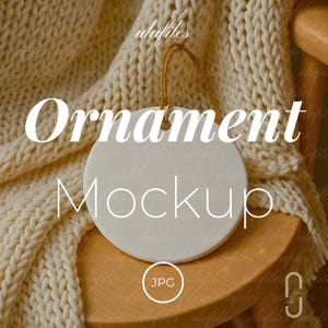 Puede incluir: Una maqueta de adorno redonda y blanca con las palabras "Ornament Mockup" en una fuente grande y elegante. El adorno cuelga de una cuerda dorada contra una acogedora manta de punto color crema y una silla de madera.