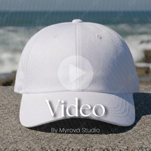 Puede incluir: Gorra de béisbol blanca con visera curva. La gorra tiene un botón en la parte superior y la palabra "Video" se muestra en la parte delantera. El texto "By Myrova Studio" está debajo. El fondo es una vista borrosa del océano.