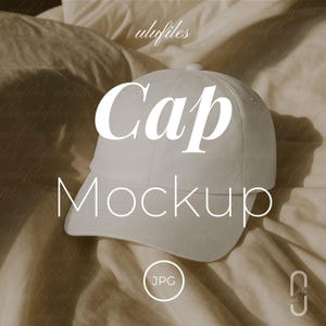 Puede incluir: Una maqueta de gorra de béisbol blanca con las palabras "Cap" y "Mockup" en letras blancas grandes. La gorra está centrada en un fondo de tela beige. La imagen incluye un icono "JPG".