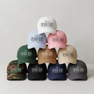Puede incluir: Una colección de gorras de béisbol en varios colores, incluyendo blanco, rosa y verde. Cada gorra presenta el texto "Your Design Here" en una fuente estilizada. Las gorras están apiladas, mostrando una variedad de opciones de diseño.
