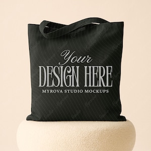 Puede incluir: Bolso tote negro con el texto "Your DESIGN HERE" en fuente serif. El bolso tiene un patrón de rayas y un asa. Las palabras "MYROVA STUDIO MOCKUPS" están debajo.