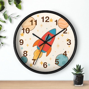 Peut inclure: Une horloge murale ronde avec un cadre noir. Le cadran de l'horloge présente une fusée de dessin animé, des planètes, des étoiles et des chiffres. La fusée est rouge, bleue et orange. Les planètes sont beiges et bleues. Les aiguilles sont noires.