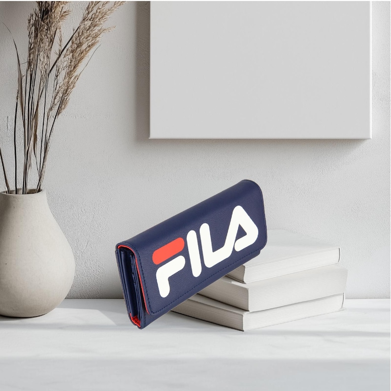 Pu&ograve; includere: Un portafoglio blu navy con la scritta "FILA" in lettere bianche e rosse. Il portafoglio &egrave; rettangolare e sembra essere in pelle. L'interno &egrave; rosso. Il portafoglio &egrave; appoggiato su una pila di libri bianchi.