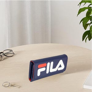 Pu&ograve; includere: Un portafoglio blu navy con il logo "FILA" bianco e rosso. Il portafoglio &egrave; rettangolare e sembra essere in pelle o un materiale simile. L'interno &egrave; rosso. Il portafoglio &egrave; su un tavolo marrone chiaro.