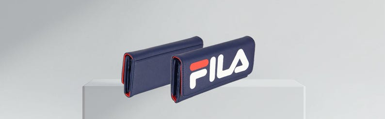 Pu&ograve; includere: Due portafogli blu navy con finiture rosse. Un portafoglio presenta il logo "FILA" bianco e rosso. I portafogli sono esposti su una superficie bianca su sfondo grigio chiaro. I portafogli sembrano essere in pelle.