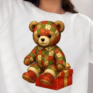 Puede incluir: Un oso de peluche con un atuendo de retazos en rojo, verde y beige, sentado sobre una caja de regalo roja con una cinta dorada. El oso tiene pelaje marrón y una nariz de botón, y lleva botas a juego.