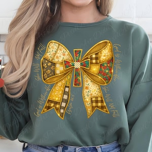 Puede incluir: Una sudadera verde con un gran lazo adornado y una cruz en el centro. El lazo está compuesto por varias telas estampadas en oro, marrón y flores. El texto alrededor del lazo dice "God is Within Her, She Will Not Fall, Salmo 46:5."