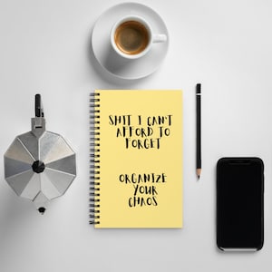 Op de afbeelding: Een geel notitieboek met een spiraalbinding. Het notitieboek heeft zwarte tekst met de tekst "Shit I can't afford to forget. Organize your chaos."
