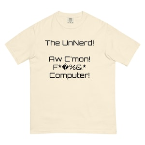 May include: A cream-colored t-shirt with the text "The UnNerd! Aw C'mon! F*?%&* Computer!" printed in black. The shirt has a crew neck and short sleeves. The fabric appears to be a soft, comfortable material.