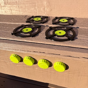 May include: Four black circular stove burner grates with bright neon yellow centers arranged in a square pattern, accompanied by four matching neon yellow ridged control knobs positioned in a horizontal row below the burner grates.