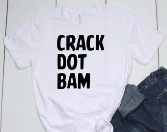 May include: White t-shirt with the words "CRACK DOT BAM" printed in bold black letters. The shirt is made of a soft material and is paired with blue denim jeans.